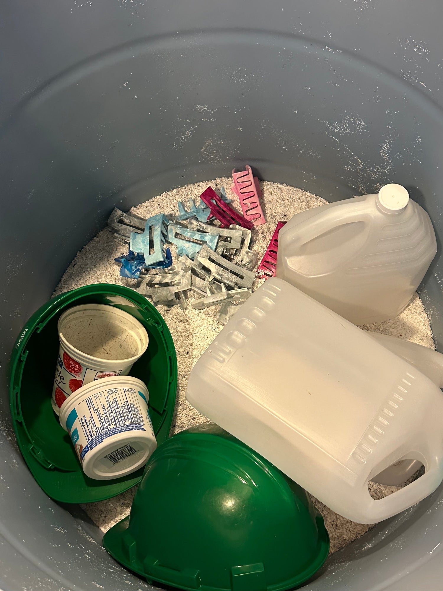 Photo d'un baril contenant des matériaux recyclables, entouré de granulés de plastique transformés et de pinces à cheveux fabriquées à partir de plastique recyclé, mettant en valeur le processus de recyclage durable et innovant d'Unique Plastique.